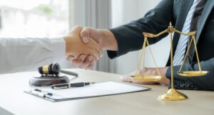 A handshake after a lawyer provides legal consultation for a business dispute, with a justice scale and gavel on the office desk.